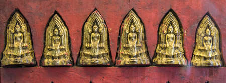 Ancient Buddha images on a red wooden wall.