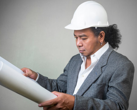 Engineer man worker with white safety uniform helmet  holding a drawing blueprint paper plan, construction process layout.の写真素材
