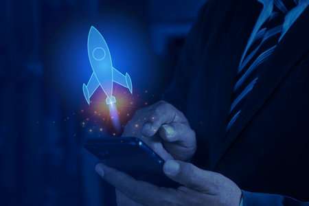 Man hand holding a smartphone, projecting a holographic rocket, on dark background. Concept of...