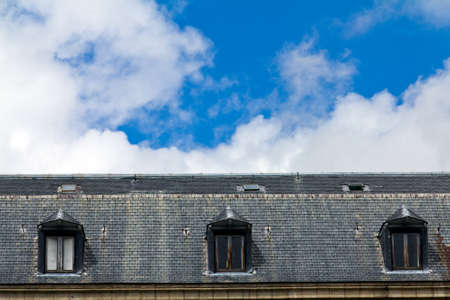 Three windows in an old roof in a sunny day with some cloudsの写真素材