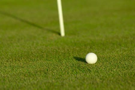 A golf ball near a hole with golf poleの写真素材