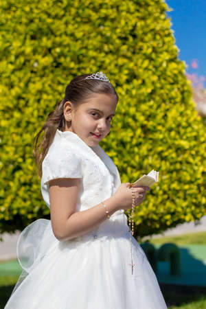 A young girl in her First Holy Communion holding a prayer book and a rosaryの写真素材