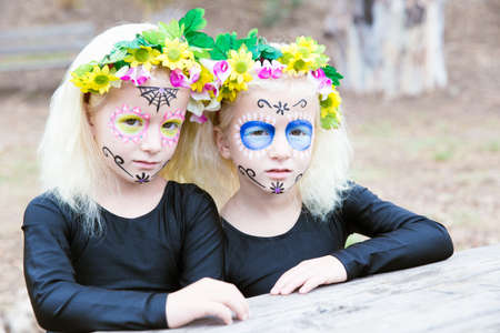 Halloween makeup. Photo of twin girls with black clothing sitting in front of a table outdoorsの写真素材