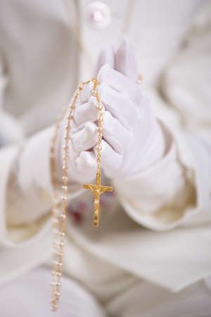 Closeup of a boy's hands with white gloves holding a gold rosary for his First Holy Communion. Shallow depth of field.の写真素材