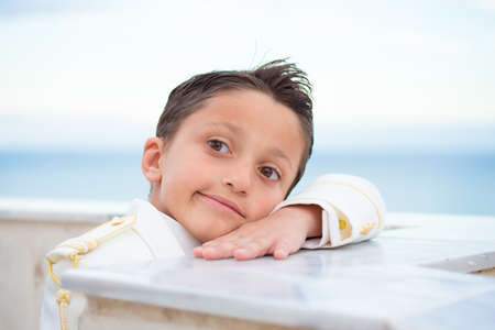 Young boy with white suit leaning on a wall with his head over his hand in his First Communion. Shallow depth of field.の写真素材