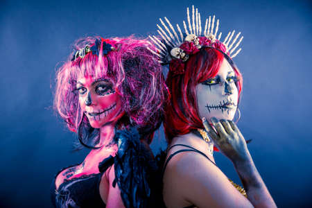 Two girls wearing Halloween costume and sugar skull makeup on a dark background