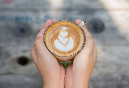 Female hands holding a cup of coffee over wooden table, top viewの写真素材