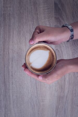 Female hands holding a cup of coffee with heart make up on face of milk cream on wooden table, top viewの写真素材