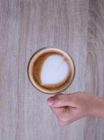 Female hands holding a cup of coffee with heart make up on face of milk cream on wooden table, top viewの写真素材
