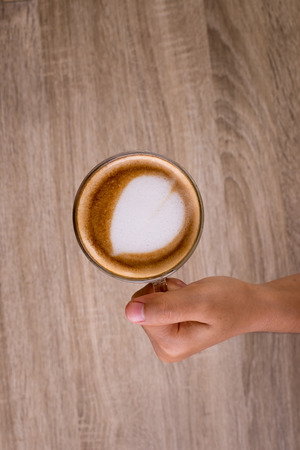 Female hands holding a cup of coffee with heart make up on face of milk cream on wooden table, top viewの写真素材