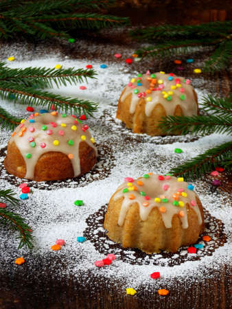 Sweet muffins decorated fondant, multicolored sprinkles. Cupcakes on dark background with spruce branches. Christmas and New Year cakes.の写真素材