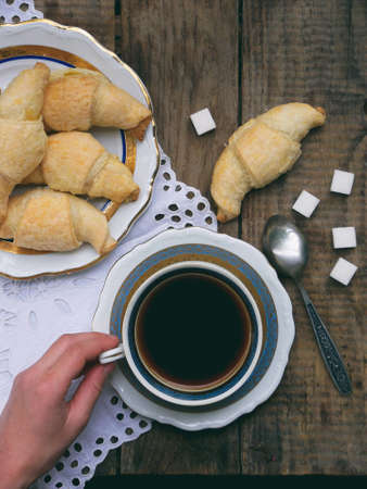 Breakfast with croissants and black coffee composition with girl hand on wooden retro background.の写真素材