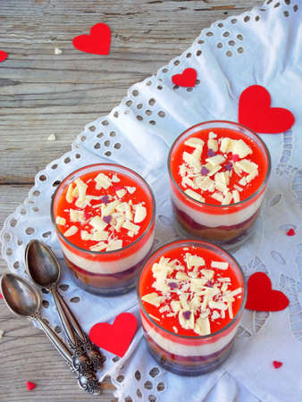 Cheesecake dessert in glass jar on wooden background: chocolate biscuit, salted caramel, strawberry jelly, cheese mousse, chocolate mirror glaze. Valentine's Day concept. Selective focus. Copy spaceの写真素材