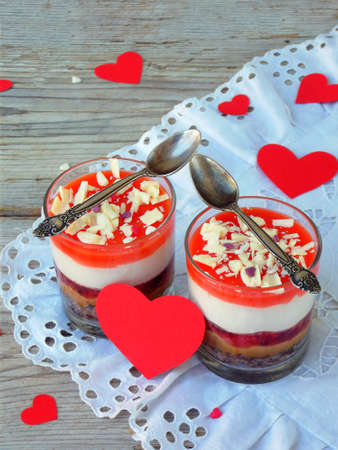 Cheesecake dessert in glass jar on wooden background: chocolate biscuit, salted caramel, strawberry jelly, cheese mousse, chocolate mirror glaze. Valentine's Day concept. Selective focus. Copy spaceの写真素材