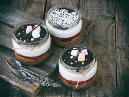 Cheesecake dessert in glass jar on wooden background.: chocolate biscuit, salted caramel, strawberry...