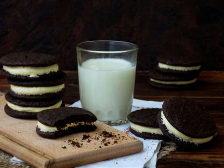 Homemade chocolate cookies with white marshmallow cream and glass of milk on dark background. Selective focus.の写真素材