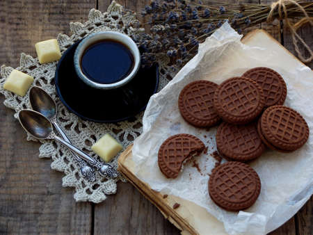 Romantic composition of chocolate cookies with white cream, cup of coffee and bouquet lavender on wooden background. Selective focus.の写真素材