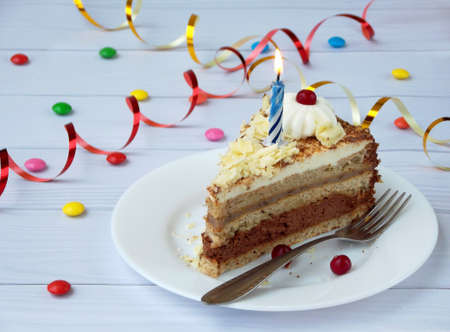 piece of chocolate banana cake decorated with rosettes of cream, berries and candles on light wooden...