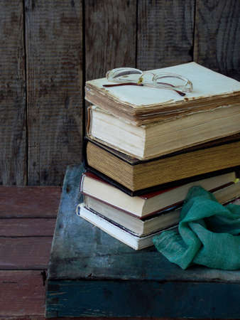 The composition of a stack of old books and glasses on a wooden background. Vintage photo. Side view.の写真素材