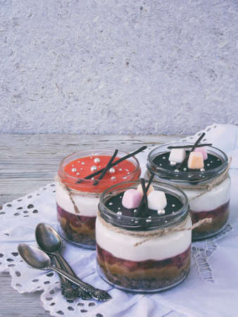Cheesecake dessert in glass jar on wooden background.: chocolate biscuit, salted caramel, strawberry jelly, cheese mousse, chocolate mirror glaze. Selective focus. Copy spaceの写真素材