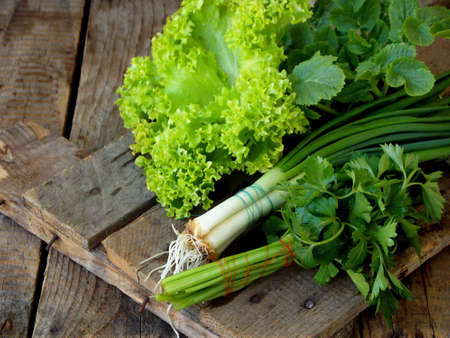 Spring green for salad on a brown wooden background. Onion, lettuce, parsley, radish leaves.の写真素材