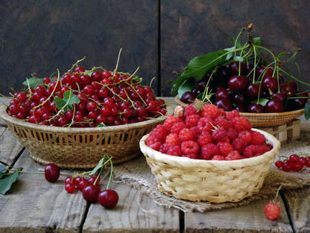 Fresh fruit and berries in baskets on wooden background - red currants, raspberries, cherries - rustic fotoの写真素材