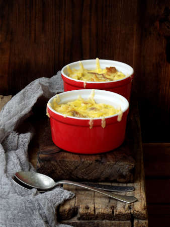 Casserole from eggs, bacon, dried tomatoes and cheese in red ramekin on brown wooden backgroundの写真素材