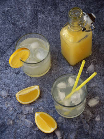 Two glasses of cold homemade lemonade with lemon slices, ice cubes and straws on dark background. Copy spaceの写真素材