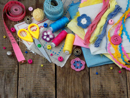 Pink, yellow and blue accessories for needlework on brown wooden background. Knitting, embroidery,...