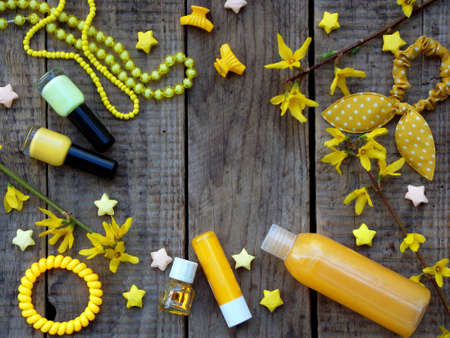 Composition of yellow accessories for young girl or teenager. Nail polishes, lipstick, hair clips, bands, beads, bracelet, perfume and flowers. Top view on wooden backgroundの写真素材