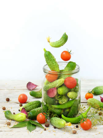 Cucumbers and cherry tomatoes with herbs and spices for pickling in glass jar with flying ingredients on a white background.の写真素材