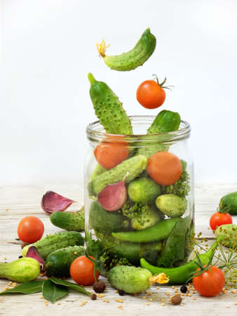 Cucumbers and cherry tomatoes with herbs and spices for pickling in glass jar with flying ingredients on a white background.の写真素材