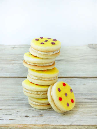 Sandwich biscuits with yellow icing sprinkled with sugar stars on light wooden backgroundの写真素材