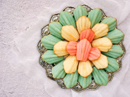 pastries of blue, pink and yellow flower on a folded metal plate on a light background. A famous French Madeleine cakesの写真素材