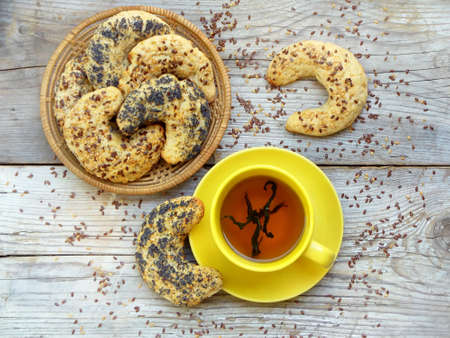 bagels sprinkled with poppy seeds and flax seeds in a basket and a yellow cup of tea on a wooden backgroundの写真素材