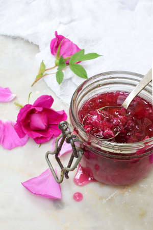 Glass jar and little spoon with tea rose petal jam on light marble background. Copy space for textの写真素材