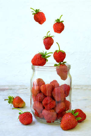 Composition of flying strawberry in jar. Cooking preparation compote or jam. Homemade conservation with organic fresh berry for the winter. Fruit dessert. Confectioneryの写真素材