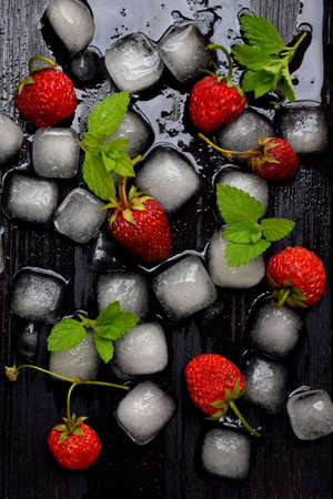 Ice cubes, strawberries and mint leaves on a black wooden background. Food backgroundの写真素材