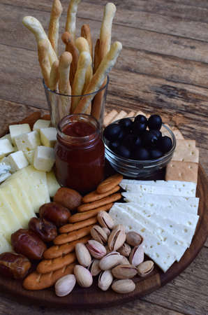Cheese plates served with grissini, crackers, dates, jam, olives and nuts on wooden background.
