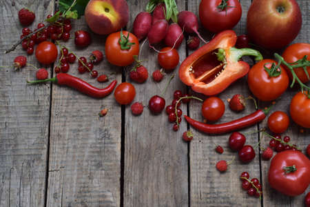 The composition of red vegetarian products: fruits and vegetables on wooden background. Apples, tomatoes, currants radishes, peppers, raspberries sweet cherry. Healthy food. Copy space for text.の写真素材