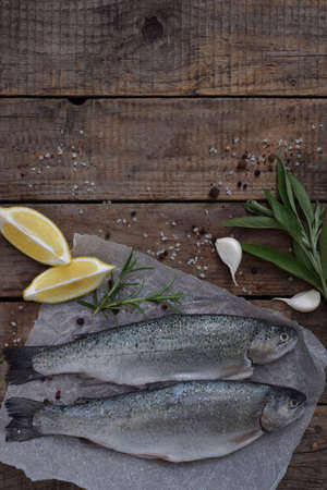 Two river trout on a board, with herbs, spices, lemon and pepper on wooden board, ready for cooking. Fresh fish.の写真素材