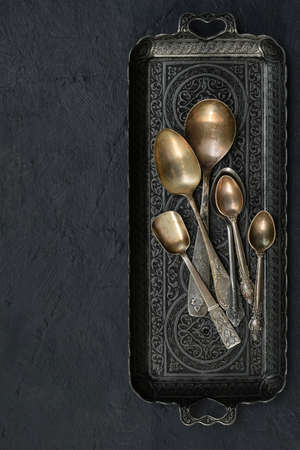 Vintage tea and dessert spoons on a metal dish on a dark concrete backgroundの写真素材