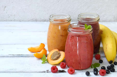 Orange, red and purple healthy smoothies of fresh ingredients - bananas, apricots, raspberries and blueberries on a light background. Copy space.の写真素材