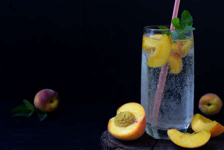 Glass of cold homemade peach lemonade or mojito cocktail with mint on dark background. Soda drink. Copy space. Photographing with natural light.の写真素材