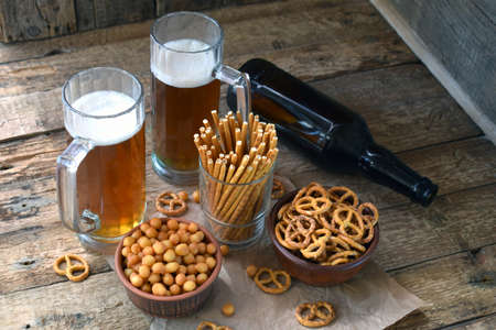 Football fan set with mugs of beer, bottle and salty snacks on wooden background. Junk food for beer or cola. Photographed with natural lightの写真素材