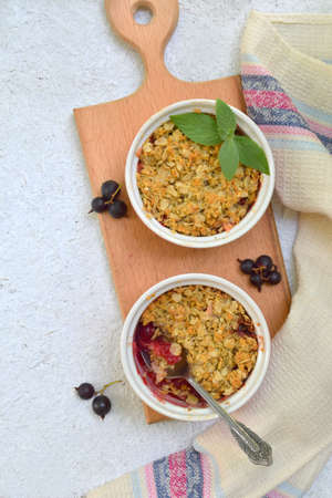 Fruits casserole or crumble with apples and berries in brown cup ramekin on light background. Copy space. Photographing with natural light.の写真素材