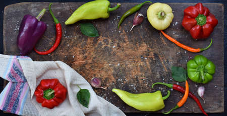 A frame for recipe from different varieties of sweet and hot pepper on a wooden background. Food border. Copy space.の写真素材
