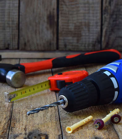 Set of tools for building and treatment on wooden background: hammer, measuring tape, drill.