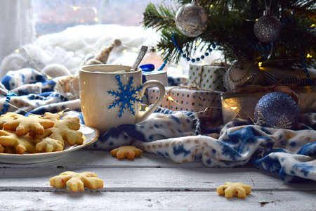 Christmas and new year holiday celebration concept background. Cup of cocoa with marshmallow, homemade chocolate cookie and peanut biscuit, lighted candles, xmas tree decoration on wooden tableの写真素材