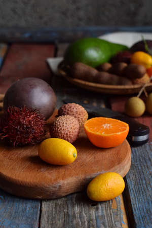 Mix of ripe tropical fruits with passion fruit, kumquat, lychee, rambutan, tamarind, avocado, coconut, dragon eye on a wooden background. Superfood background. Vegetarian food.の写真素材